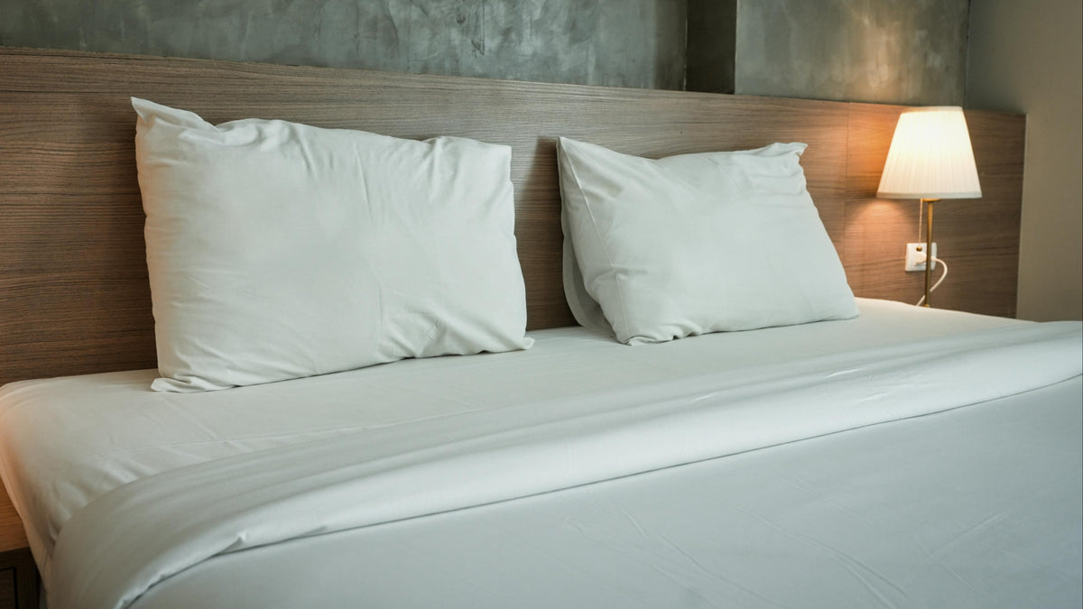 Bed with white pillows and a lamp on a nightstand in a bedroom setting.